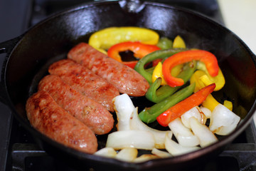 Sausage cooking on the stove in a cast iron skillet with bell peppers and onion.