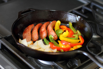 Sausage cooking on the stove in a cast iron skillet with bell peppers and onion.