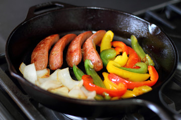 Sausage cooking on the stove in a cast iron skillet with bell peppers and onion.
