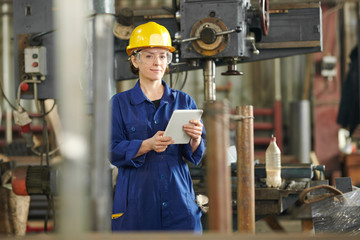 Waist up portrait of smiling female worker wearing hardhat looking at camera while standing by...
