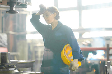 Waist up portrait of exhausted woman working at factory, wiping sweat standing in sunlight, copy...