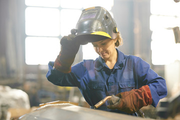 Waist up portrait of smiling woman welding metal while working at industrial plant, copy space - Powered by Adobe