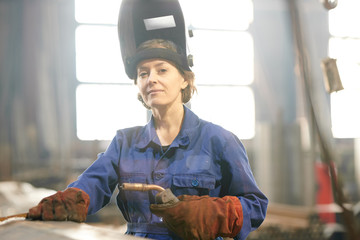 Waist up portrait of smiling female welder posing confidently while working at industrial plant or in garage, copy space - obrazy, fototapety, plakaty