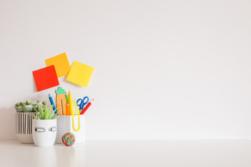 Creative desk with school supplies and white wall for copy space.