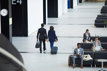 Rear view of business people in formal jackets carrying luggage and going to board plane while...