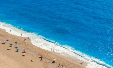 Top view of beach with cyan blue water and people swimming and sunbathing.