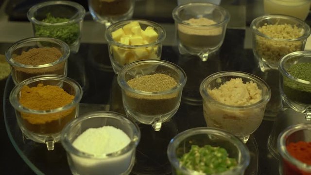 A steady, extreme close up shot of many small glass containers with diverse spices.