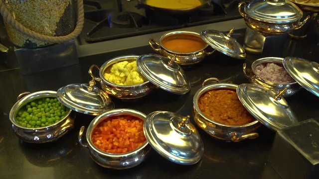 A steady, medium shot of small silver pots which contain different fresh or cooked vegetables.