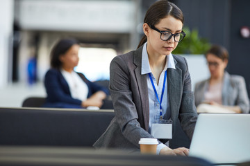 Serious concentrated female conference participant in glasses wearing badge on neck sitting in...