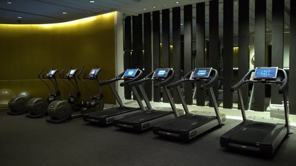 A steady, wide shot of a fully equipped gym with elliptical bicycles.