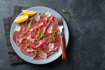 Marbled beef carpaccio with arugula, lemon and parmesan cheese on dark concrete table. Top view, flat lay with copy space