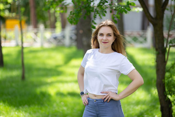 Happy smiling blonde girl-student in white t-shirt and blue jeans look at camera in the sunny park. Style clothing emotional smiling portrait.