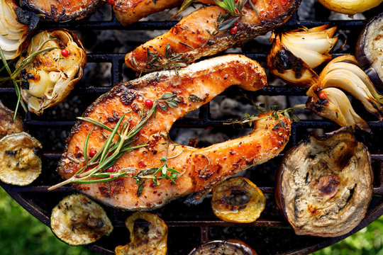 Grilled fish, grilled salmon steak with the addition of rosemary, aromatic spices and vegetables on the grill plate outdoors, top view, close-up. Grilled seafood