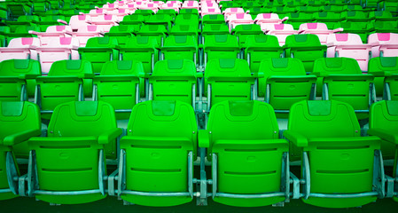Empty beautiful plastic bright green and pink stadium seats rows in a soccer stadium. Colourful weathered chairs.
