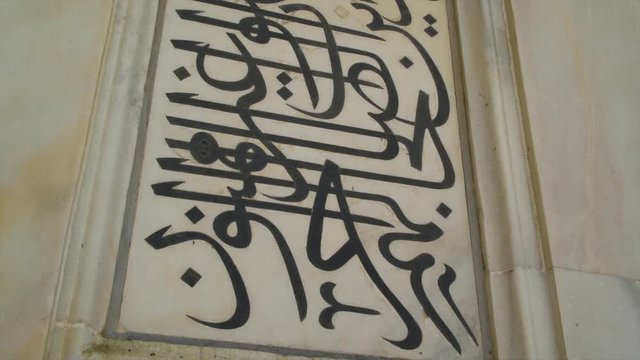 A hand held, extreme close up shot of black Arabic letters painted on white marble.