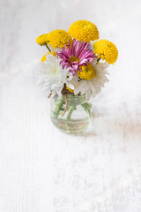 Spring flowers bouquet in a jar vase on a white wood rustic background