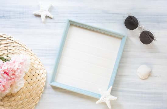 top view of summer blue picture frame with sunglasses and seashell and star fish and pink flower decoration on white wood table.summer vacation