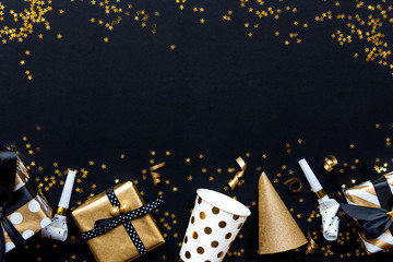 Gift boxes in various gold pattern wrapping papers and party accessories over star shaped golden sequins on a black background.