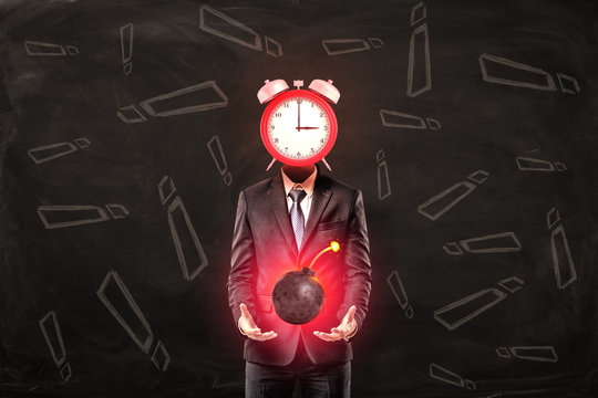 Businessman with clock instead of head holding ball bomb with fuse on black background with exclamation sign pattern