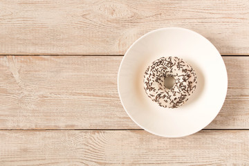 Fresh glazed donut with chocolate sprinkles on a white plate.