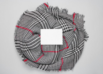 Fashionable female scarf with a white sheet of paper in the middle for copy space on a gray background. Autumn time. Top view