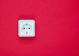 White plastic power socket on red background. Wall with copy space. Minimalism