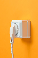 White cable plugged into power outlet on orange wall background