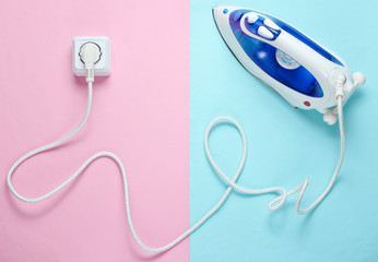 Cable Iron for ironing things plugged into power outlet in pastel background. Top view, minimalism