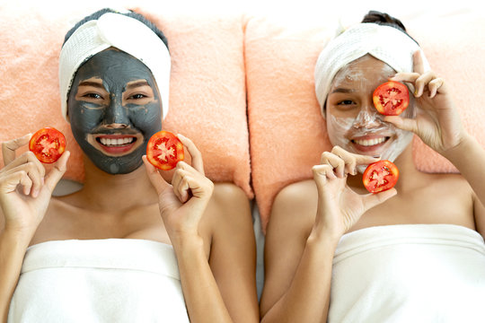 Image of two young happy women friends white bathrobes. They are take a rest and applying pieces of tomatoes to their eyes in spa salon environment. spa beauty treatment, skin care concept.