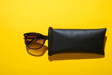 Fashionable sunglasses in protective case on yellow background. Top view