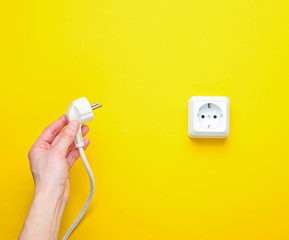 Female hands plug in power plug into electro outlet on yellow background. Minimalism. Top view