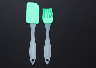 Silicone kitchen tools (spatula, brush) on a black background. Top view.