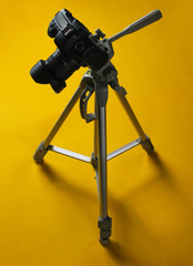 Modern digital camera with tripod on a yellow background. Minimalism