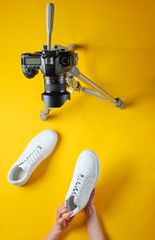 Women reviews new white sneakers with camera on tripod on yellow background. Top view. Minimalism
