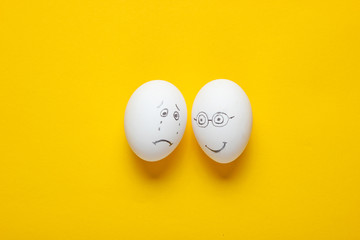 Sad and happy face eggs on yellow background. Top view