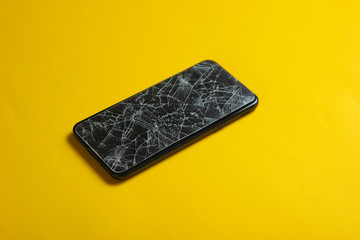 Smartphone with broken protective glass on yellow background.