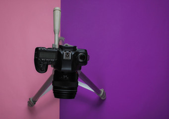 Modern digital camera with a tripod on a purple pink background. Top view. Minimalism