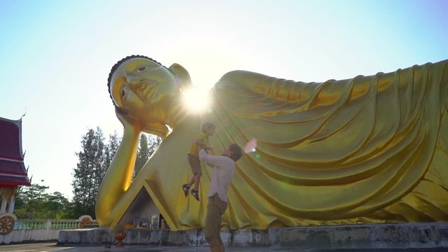 Slowmotion shot of a young man and his little son having fun in front of a statue of the lying Buddha on Phuket island. Travell to Thailand concept