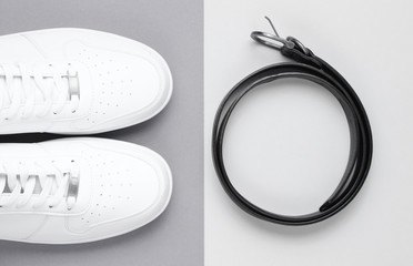 Minimalism fashion. White sneakers, leather belt on a gray background. Top view