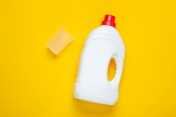 Bottle of washing gel, empty measuring container on yellow background. Top view