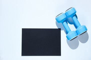 Black sheet of paper for copy space, plastic dumbbells on a gray background. Creative fitness background