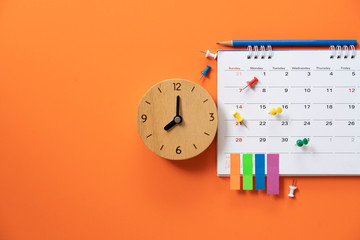 close up of alarm clock and calendar on the orange table background, planning for business meeting or travel planning concept