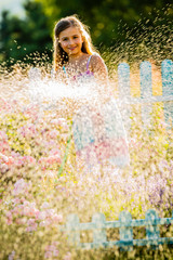 Playfull girl watering flowers with rain in the garden at summer day. Child using garden hose on...