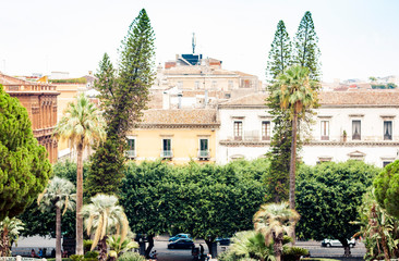 Obraz premium Traditional architecture of Sicily in Italy, typical street of Catania, facade of old buildings with tree alley.