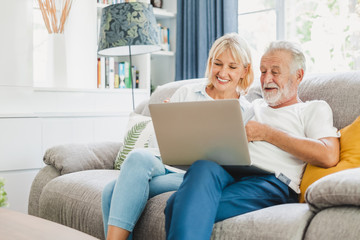 Couple senior using computer laptop on sofa at home for online shopping, surfing internet - Powered by Adobe