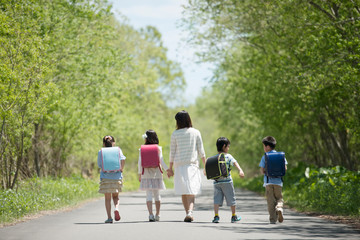 一本道を歩く小学生と先生の後姿