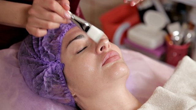 Anti-aging face treatment with a womans face mask. The cosmetologist puts a moisturizing gel on the face with a brush. A clear liquid with collagen, beauty vitamins