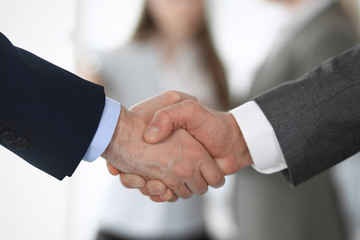 Business people shaking hands at meeting or negotiation, close-up. Group of unknown businessmen and women in modern office at background. Teamwork, partnership and handshake concept