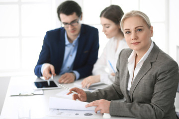 Fototapeta premium Headshot of business woman at negotiation. Group of business people discussing questions at meeting in modern office. Teamwork, partnership and business concept