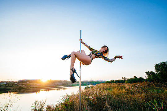 Contrast silhouette photos at sunset against the sky: girl poledancer performs an element on the pole with the split